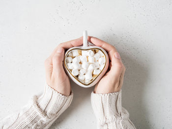 Female hands hold white ceramic cup in the form of heart with hot drink and marshmallows 