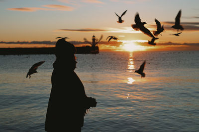 Silhouette woman with arms raised against sky during sunset