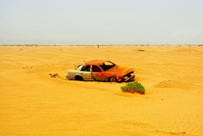 Car on desert land against clear sky