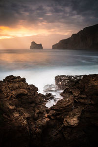 Rock formation in sea against sky during sunset