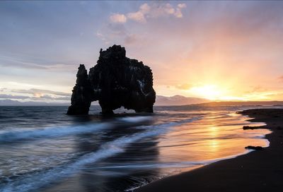 Rock formation on beach against sky during sunset