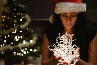 Portrait of young woman holding illuminated christmas tree at night