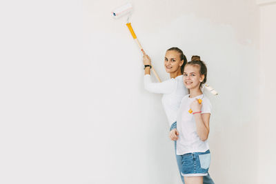 Beautiful and happy mom and daughter paint the walls in the apartment white.