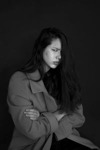 Portrait of angry woman sitting against black background