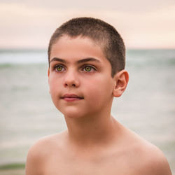 Close-up of thoughtful shirtless boy looking away while standing at beach