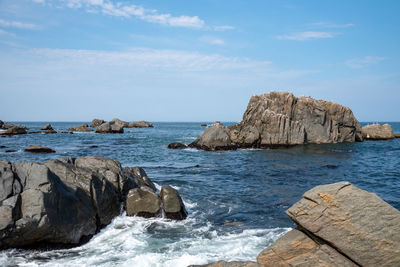 Lots of seagulls stand on rocks isolated in the ocean, relaxing and flying around the rocks.