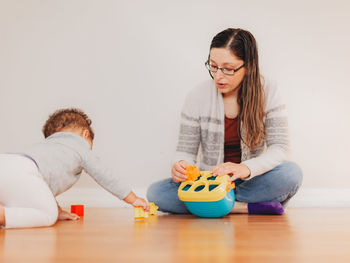 Cute boy playing with toy while sitting on floor with mother at home