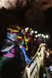 Back view group of unrecognizable travelers in warm clothes and protective helmets walking on wooden footbridge during hiking trip in cave in iceland