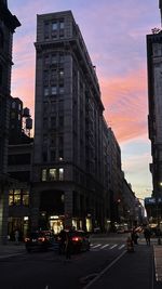 City street by buildings against sky during sunset