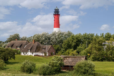 Lighthouse amidst trees and buildings against sky