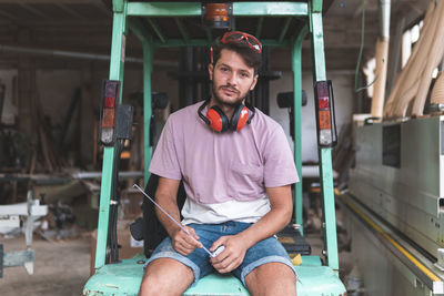 Male carpenter sitting on forklift holding tape measure in workshop