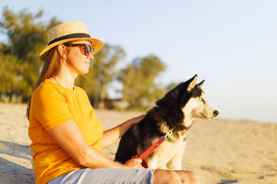 Side view of young woman with dog sitting at beach