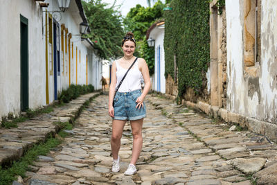 Portrait of smiling young woman standing on footpath