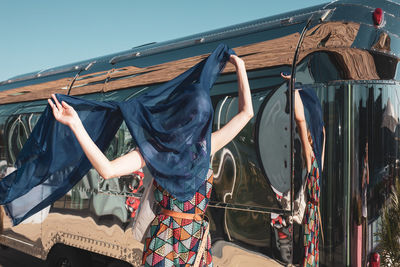 Woman holding blue scarf standing against bus