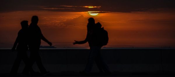 Silhouette people standing at beach during sunset