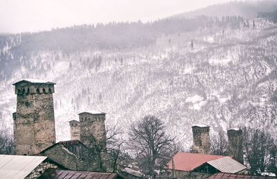 Houses and trees by building against sky during winter