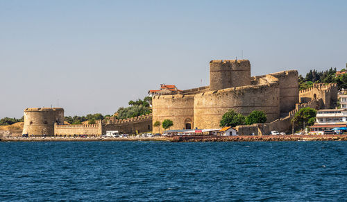 Buildings by sea against clear sky