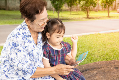 Grandmother using smart phone while sitting with granddaughter at park