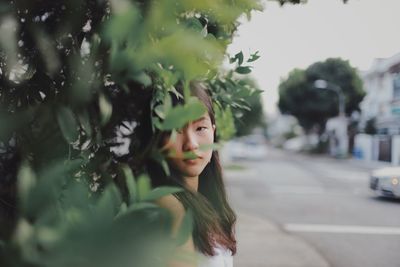 Portrait of young woman by road seen through leaves