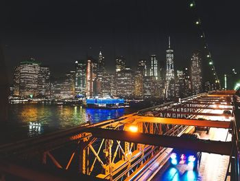 Illuminated modern buildings by river against sky at night