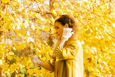 Mature woman holding mirror standing against autumn tree