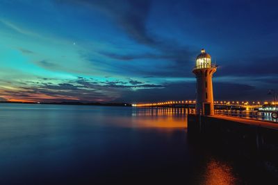 Illuminated lighthouse by sea against sky at dusk