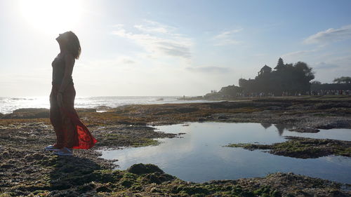 Side view of woman standing on beach against sky