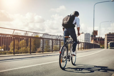 Rear view of businessman riding bicycle on bridge in city