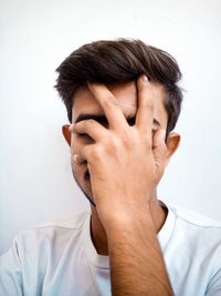 Portrait of a young man covering face against white background