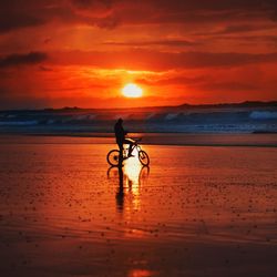 Man riding bicycle on beach against sky during sunset