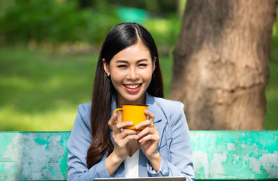 Portrait of smiling young woman holding smart phone outdoors