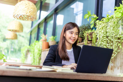 Portrait of smiling young woman using phone while sitting on table