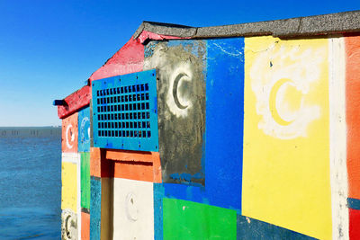 Multi colored built structure by sea against blue sky
