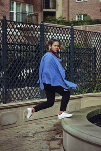 Portrait of young woman standing on railing against fence