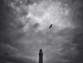 Low angle view of bird flying against cloudy sky