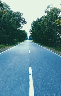 Empty road amidst trees against sky