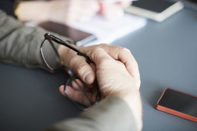 Cropped hands of businessman holding eyeglasses at desk in creative office