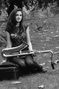 Portrait of smiling young woman holding saxophone while sitting on field