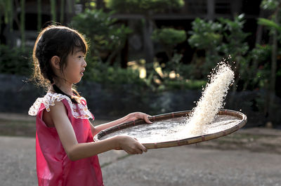 Side view of girl cleaning rice on wicker container