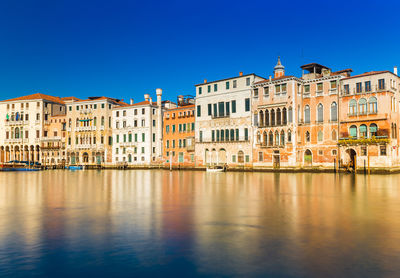 Buildings by river against clear blue sky