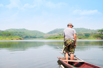 Rear view of man fishing in lake against sky