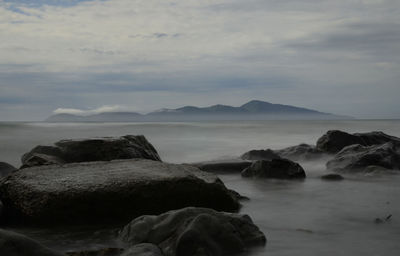 Rocks on shore by sea against sky