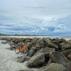 Bicycle on rock by sea against sky