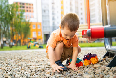 Little toddler boy playing with cars on pebbles on the playground. boy two or three years old.