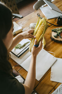 High angle view of female food stylist examining fresh corn at table in studio