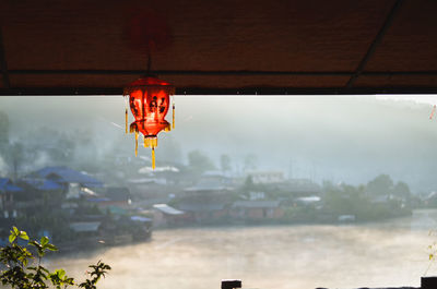 Close-up of illuminated lighting equipment hanging by building against sky