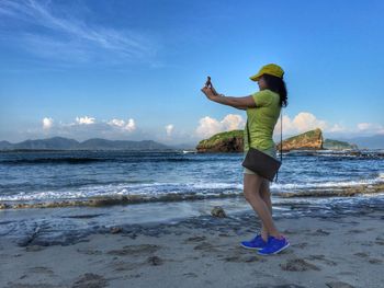 Side view of young woman taking selfie at beach against sky