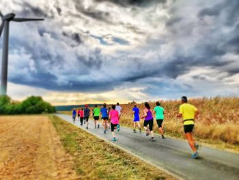 Rear view of people running on road against cloudy sky
