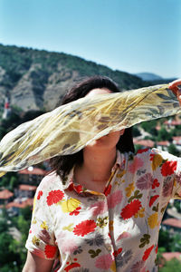 Rear view of woman holding hat against sky