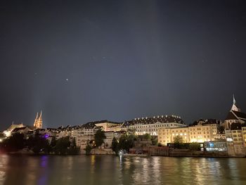 Illuminated buildings by river against sky at night